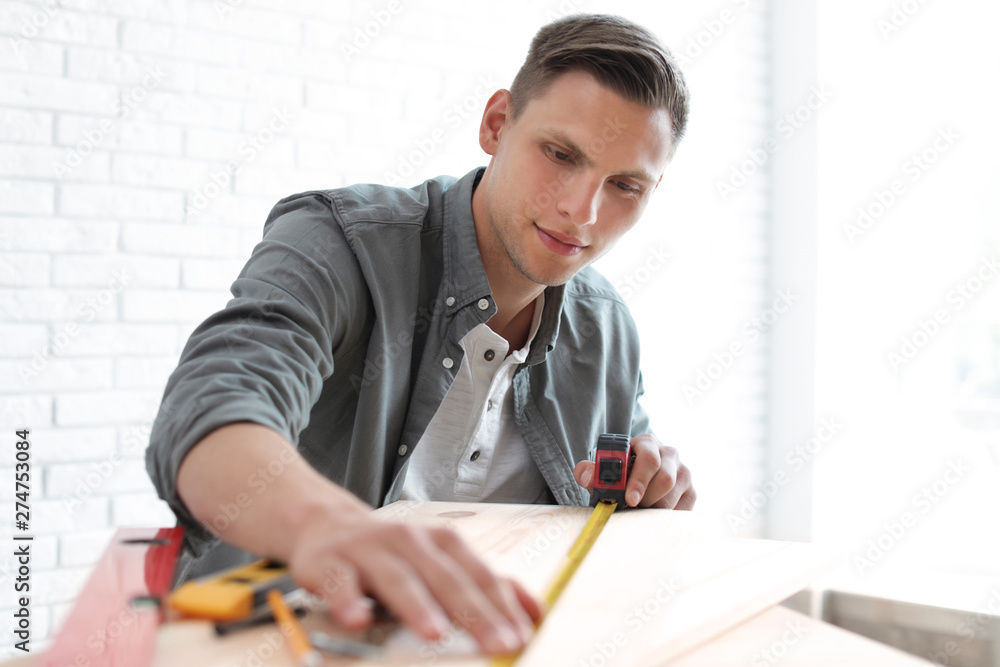 Young man working with measuring tape indoors Young man working with measuring tape indoors
