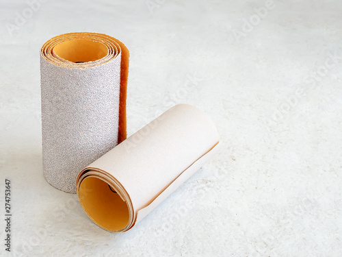Two rolls of extra coarse and super fine aluminum oxide sandpaper on a white rough textured background. Abrasive paper for dry sanding. Processing wood and metals, furniture production.