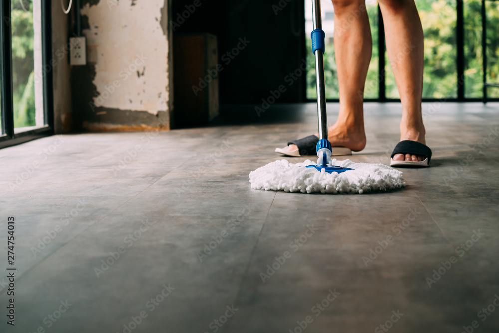 Fototapeta premium Low section of human legs and feet wearing slippers using mopping tool to clean up inside the living room at home - cleanliness housekeeping concept