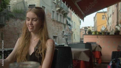  Beautiful young girl sitting in a small cafe on the canal in Venice.