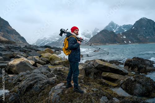 Young man photographer standing at rock in the mountains at Beach photographing the landscapes on Lofoten Islands in Norway.