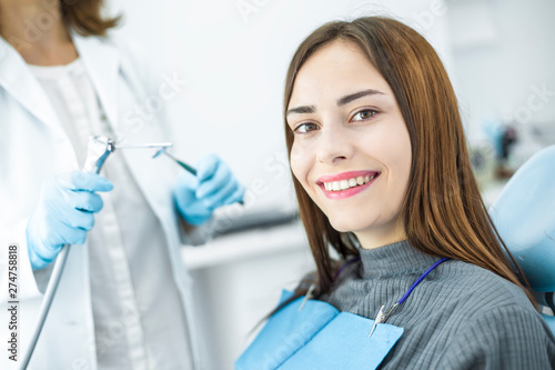 A woman is smiling with white and healthy teeth while sitting in a dental chair. Doctor dentist and happy patient in the office of a medical clinic.