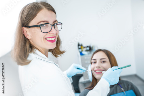 A female doctor is a dentist and the patient is smiling with healthy and white teeth. 