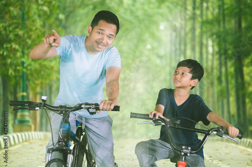 Asian man riding a bicycle with his son in the park