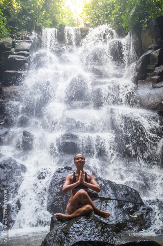 Woman practices yoga near waterfall in Bali  Indonesia