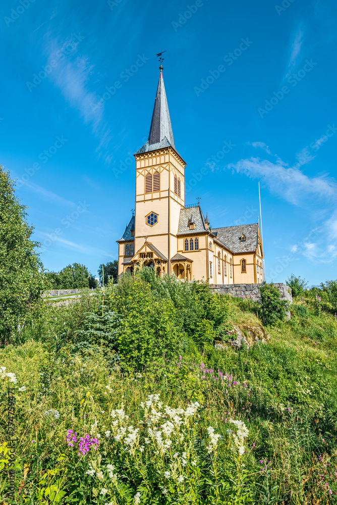 View at Vagan Church, called Lofoten Cathedral, from the slope covered with green plants and flowers. Kabelvag village in Austvagoya island, Nordland, Northern Norway.