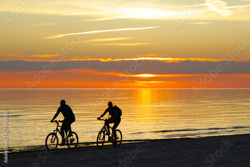 couple riding a bicycles and sunset over the sea on background © Iveta