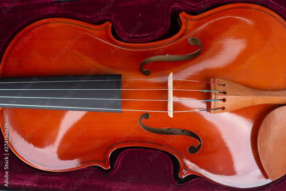 Part of an orange violin in a burgundy velvet case. Part of an orange violin in a burgundy velvet case.