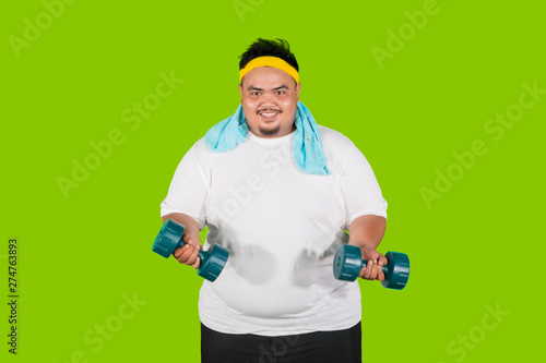 Fat man exercises biceps with dumbbells on studio