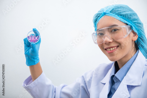 Young attractive female scientist with protective eyeglasses and mask holding a transparent pill with fingers in gloves in the pharmaceutical research laboratory