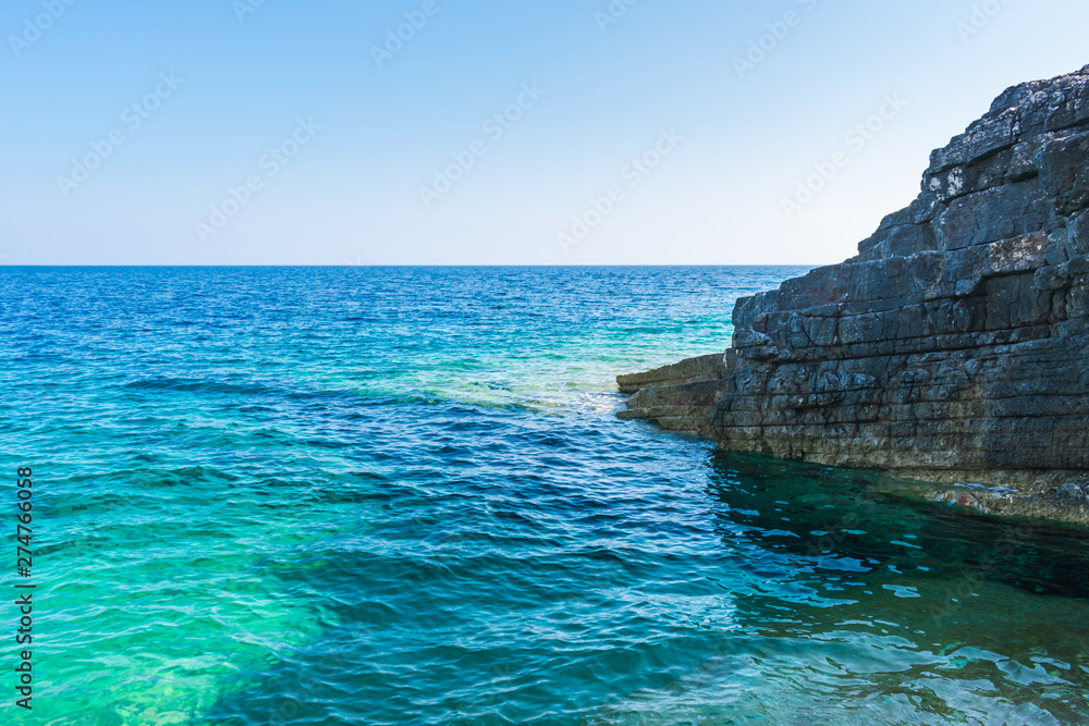 View of a cliff in the clear blue and turquoise water shielding a small rocky beach, Vis island, travel Croatia