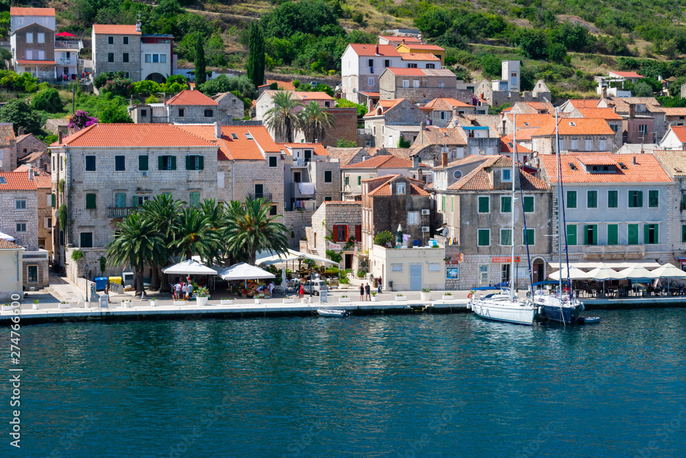 Old city of Vis viewed from the sea entering the harbor with old stone houses with red rooftops and sailing boats anchored in summer, Vis island, Croatia
