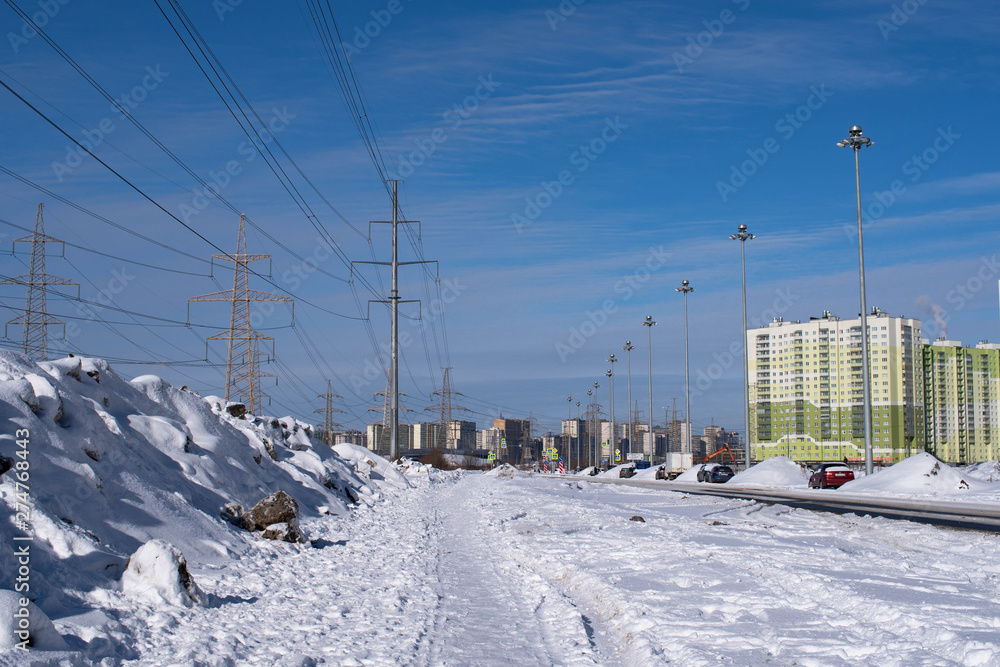 Obraz premium power transmission towers on the background of residential high-rises in the winter landscape