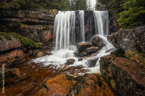 Amazing waterfall in the middle of mountain forest. River full of water during spring  beautiful flowing mass. Lovely contrast of water and surrounding forest green. Stones and fresh green leaves.