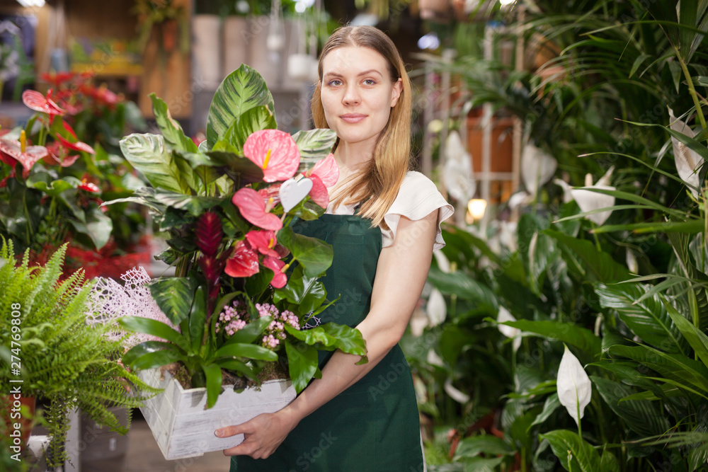 Female seller wearing an apron and happily standing among flowers in floral shop