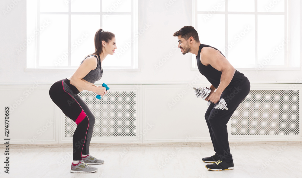 Sporty couple working out with dumbbells in front of each other Sporty couple working out with dumbbells in front of each other