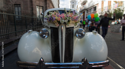 Arrangement of red and yellow roses on the hood of an old white car parked on a street full of people walking