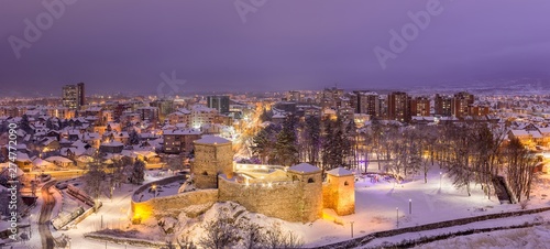 Wide panorama of snow covered beautiful Pirot cityscape during night, city lights and Christmas decoration