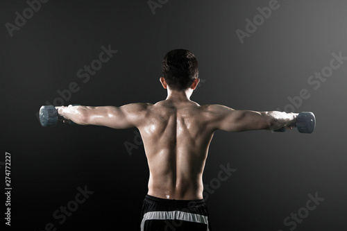 Rear view of shirtless young man lifts dumbbells