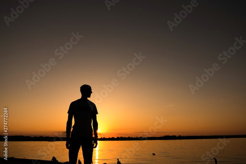 The young man is standing before the river bank with yellow Sunrise or sunset
