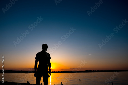 The young man is standing before the river bank with yesllow - blue Sunrise or sunset