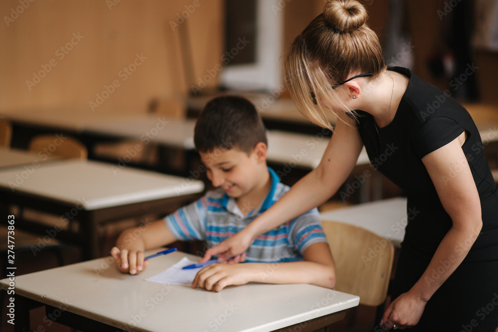 Teacher helping school kids writing test in classroom. education, elementary school, learning and people concept Teacher helping school kids writing test in classroom. education, elementary school, learning and people concept