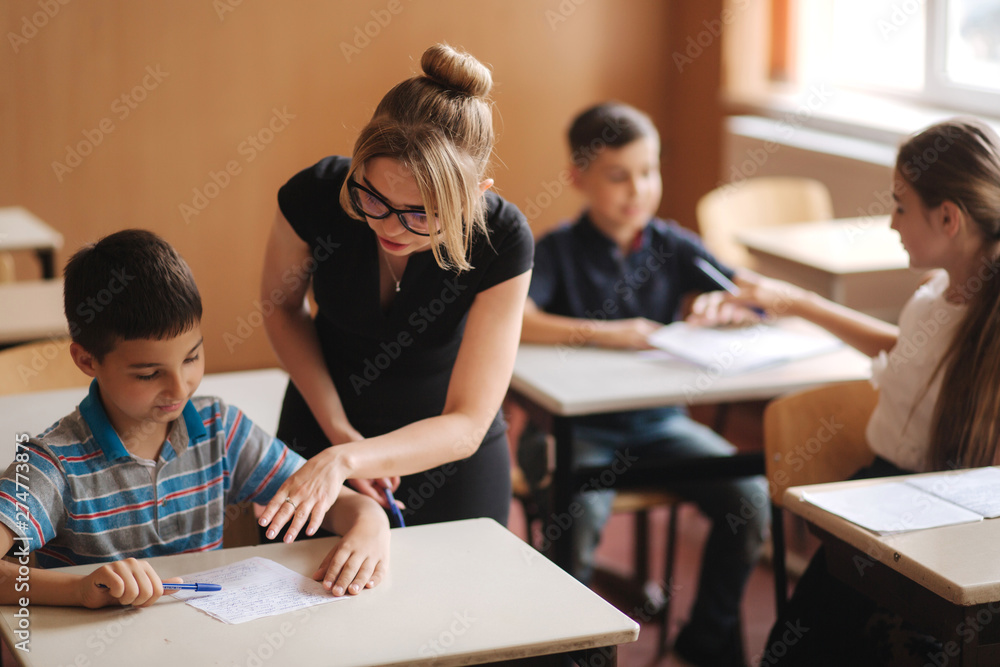 Obraz premium Teacher helping school kids writing test in classroom. education, elementary school, learning and people concept