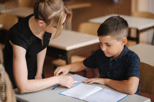 Teacher helping school kids writing test in classroom. education, elementary school, learning and people concept