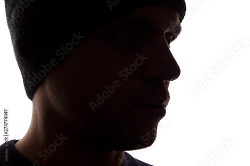 Portrait young man, unshaven, side view in cap - dark silhouette