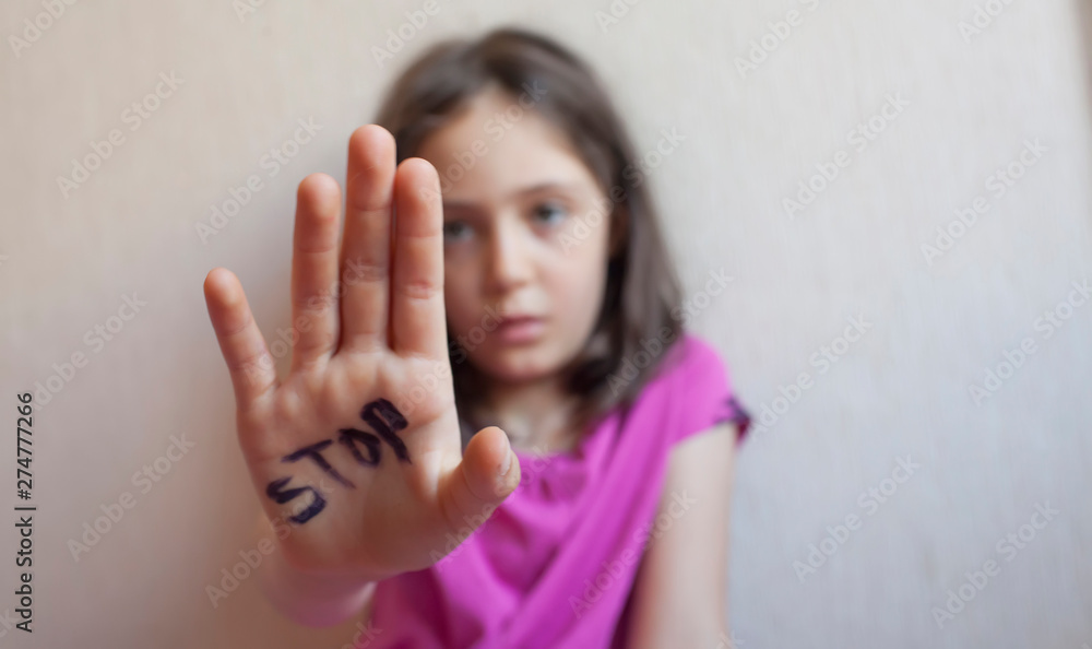Little girl protects herself with a hand on the palm of her inscription "stop" - obrazy, fototapety, plakaty 
