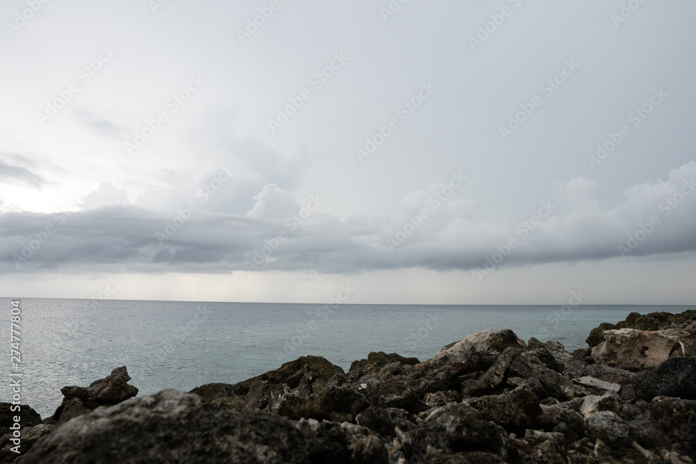 In the foreground is a rocky shore. In the distance, the ocean and clouds.
