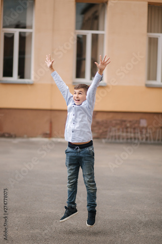Happy boy jump and raises hands up. Background of school