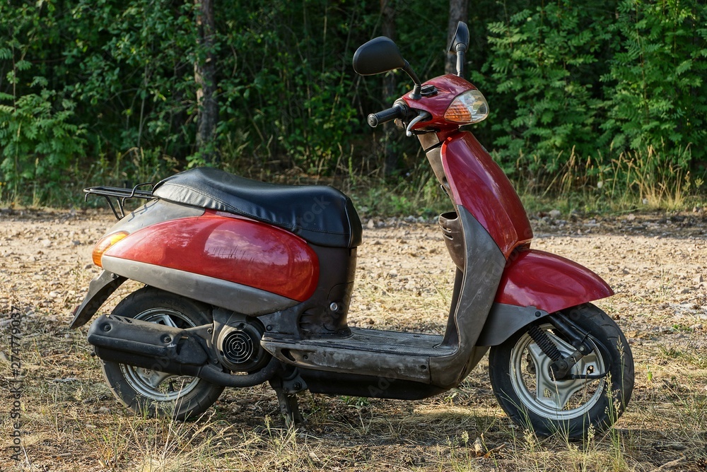 Fototapeta one old red scooter stands in the grass in the park