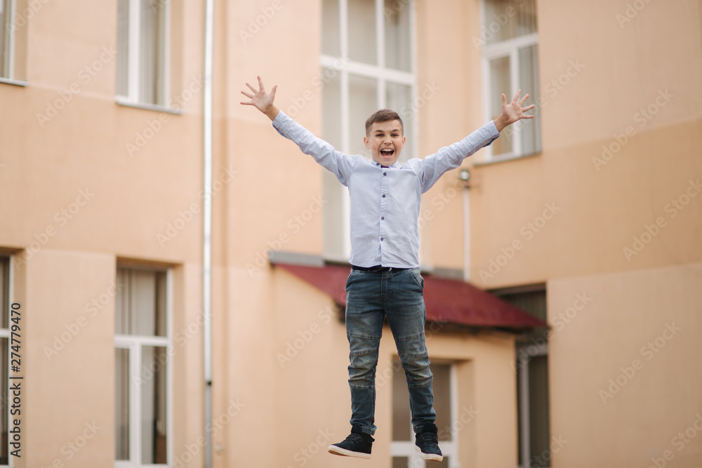 Happy boy jump and raises hands up. Background of school