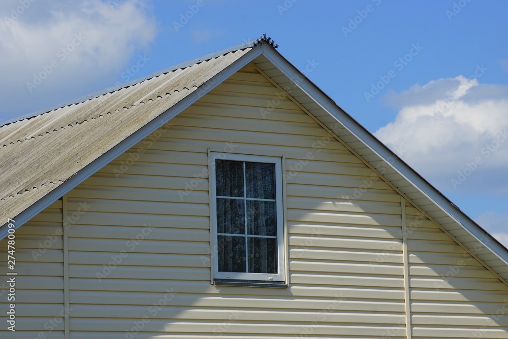 attic of a gray house with a small window against a blue sky and clouds