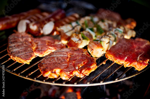 Different types of juicy meats on hot coals on grill in garden