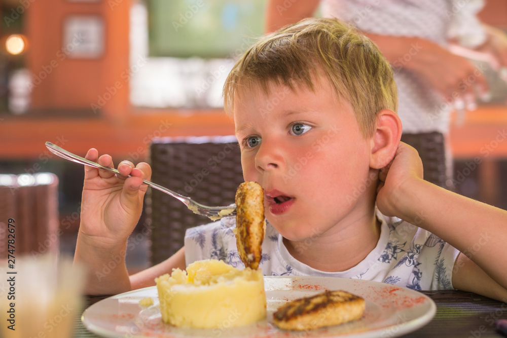 A little boy of 5-6 years old is eating mashed potatoes and a cutlet in a restaurant. A little boy of 5-6 years old is eating mashed potatoes and a cutlet in a restaurant.