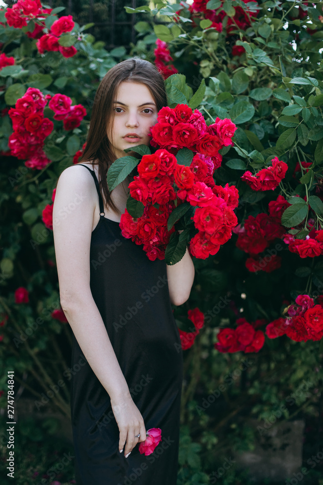 Close up summer portrait of young sensual interesting pretty young woman outdoors near red roses. Modeling, fashion, trends, nature concept Close up summer portrait of young sensual interesting pretty young woman outdoors near red roses. Modeling, fashion, trends, nature concept