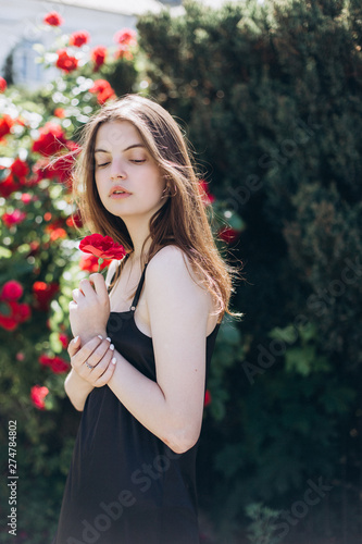 Close up summer portrait of young sensual interesting pretty young woman outdoors near red roses. Modeling, fashion, trends, nature concept