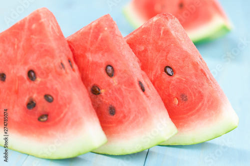 Fresh juicy watermelon slices photographed on blue wood (Selective Focus, Focus on the front of the third melon slice)