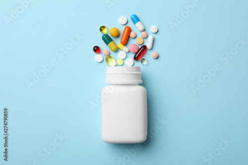 Bottle and scattered pills on color background, top view photo