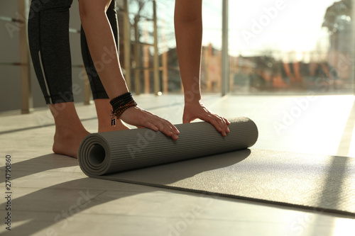 Young woman rolling yoga mat in sunlit room, closeup