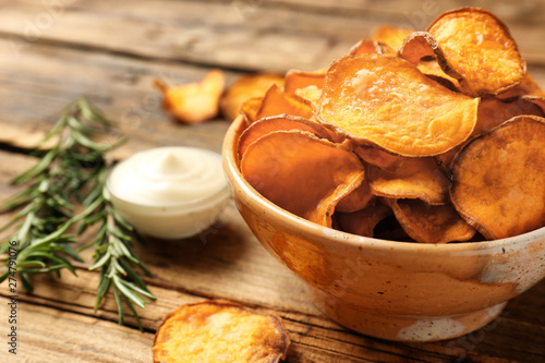 Delicious sweet potato chips in bowl, rosemary and sauce on table. Space for text photo