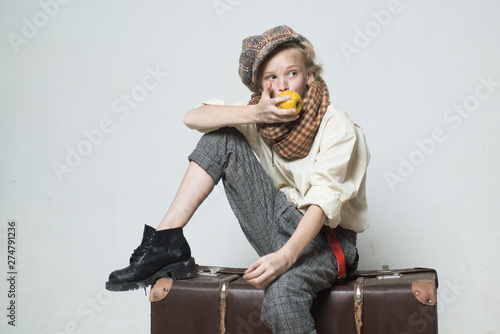 Travel with old suitcase. Homelss. old fashioned child in beret eat apple. retro fashion model. Vintage suspender. teen girl in retro male suit. street kid with dirty face. vintage english style