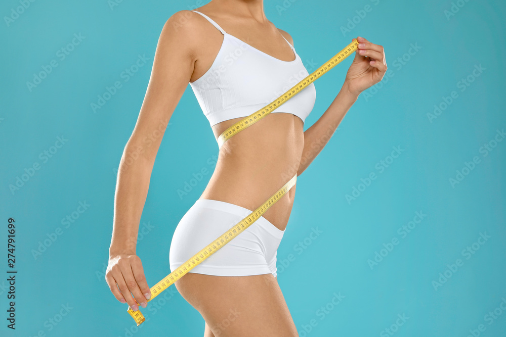 Slim young woman with smooth gentle skin in underwear measuring body on color background Slim young woman with smooth gentle skin in underwear measuring body on color background
