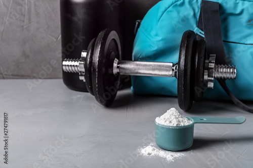 Composition with protein powder and dumbbell on table. Space for text