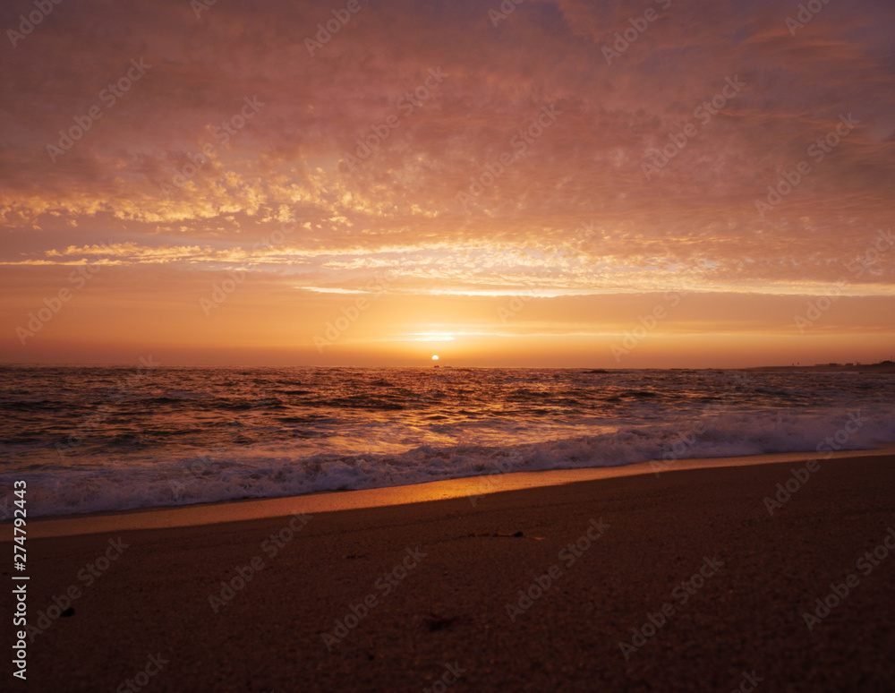 Beautiful vivid sky at sunset on the beach as waves break on shore