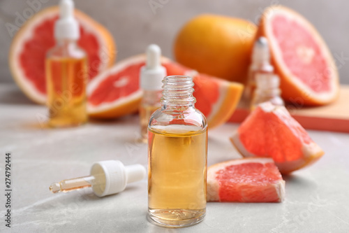 Bottles of essential oil and fresh grapefruits on grey table