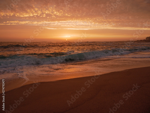Big waves break on beach at sunset in Portugal with beautiful sky