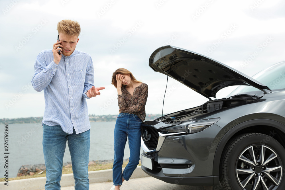 Young man and woman near broken car outdoors Young man and woman near broken car outdoors